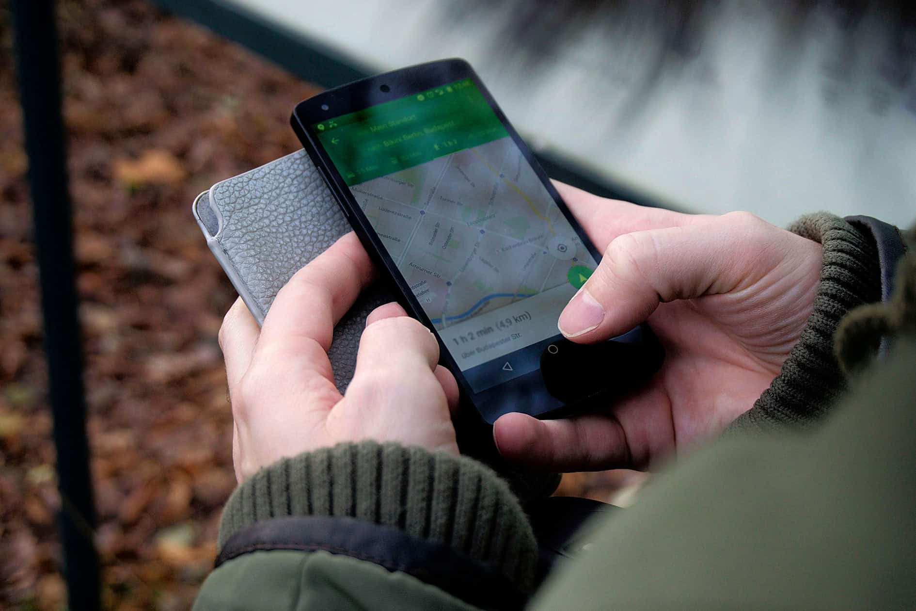 Persoană folosind aplicația AgroMonitoring pe un smartphone Android negru, subliniind monitorizarea în timp real a utilajelor agricole prin GPS.