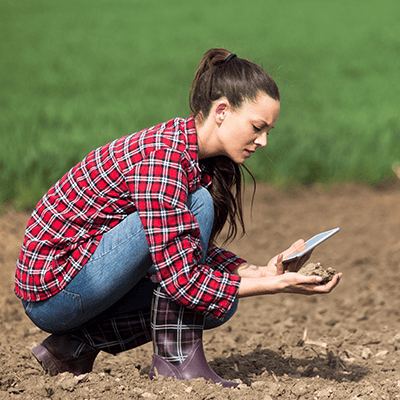Tânără fermieră verificând calitatea solului cu o tabletă pe câmp.